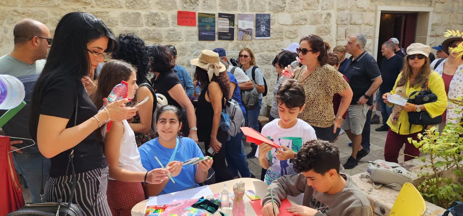 ילדים ומבוגרים יוצרים בנייר צבעוני סביב שולחן בחצר